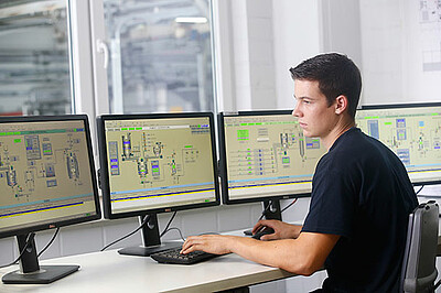Ein Mitarbeiter kontrolliert die Papiermaschinen an mehreren Monitoren in einer Warte